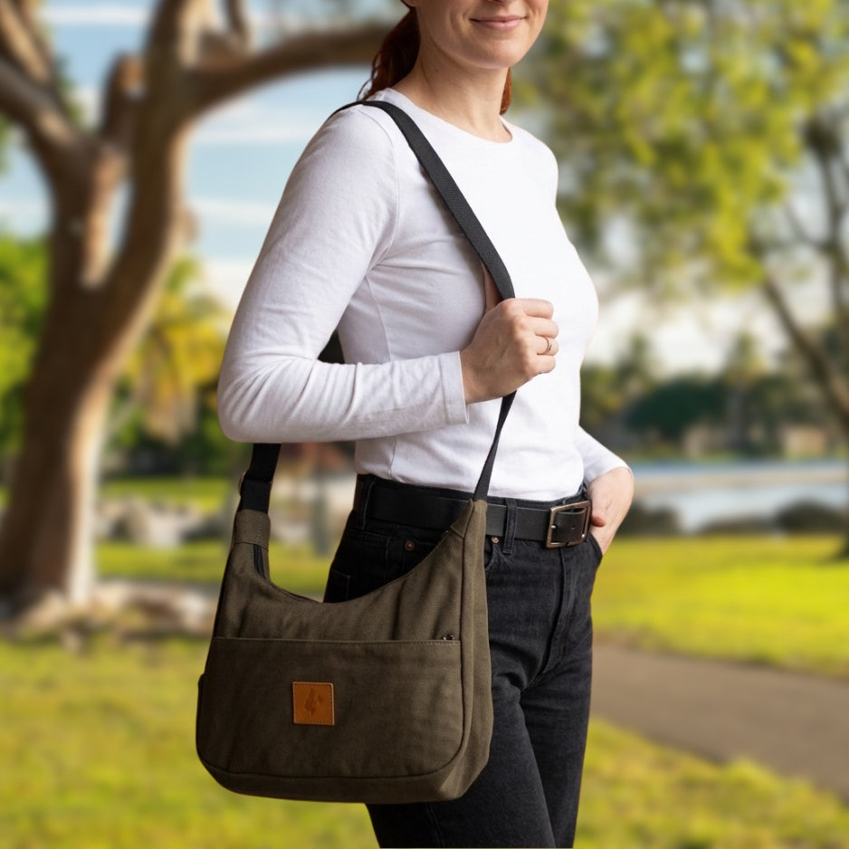 Woman holding a brown shoulder bag outdoors with greenery in the background